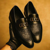 Black Gucci loafers held by a gloved hand against a brown background